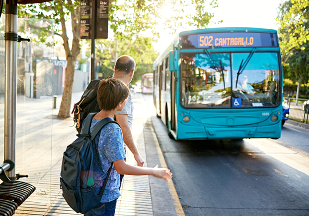 Man and young son standing at bus stop as vehicle approaches
